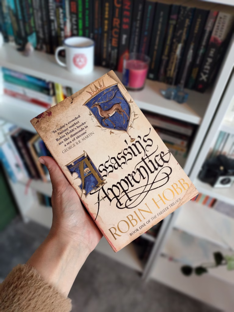 A hand holding Assassin's Apprentice by Robin Hobb